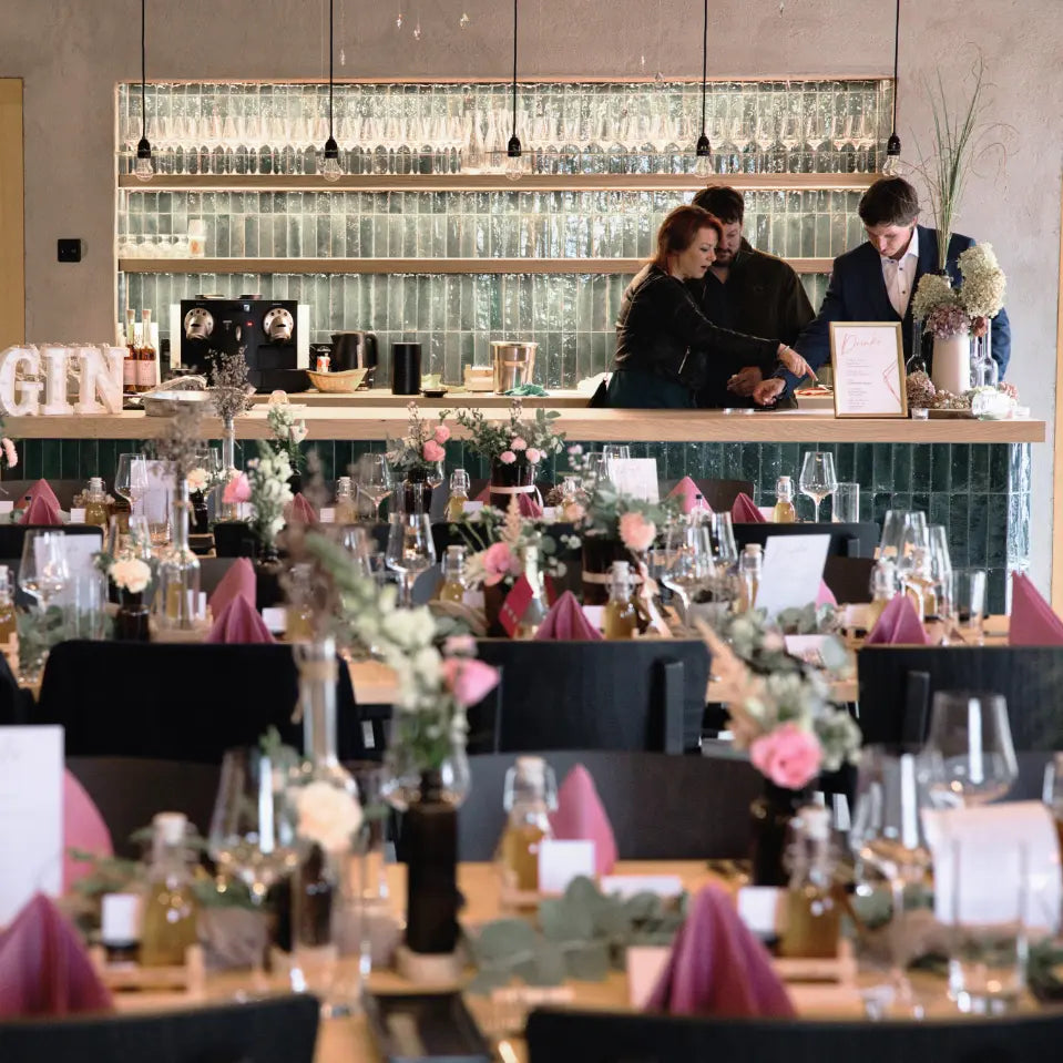 Festlich gedeckter Veranstaltungsraum mit langen Tischen, Blumendekoration und Bar im Weingut Marugg