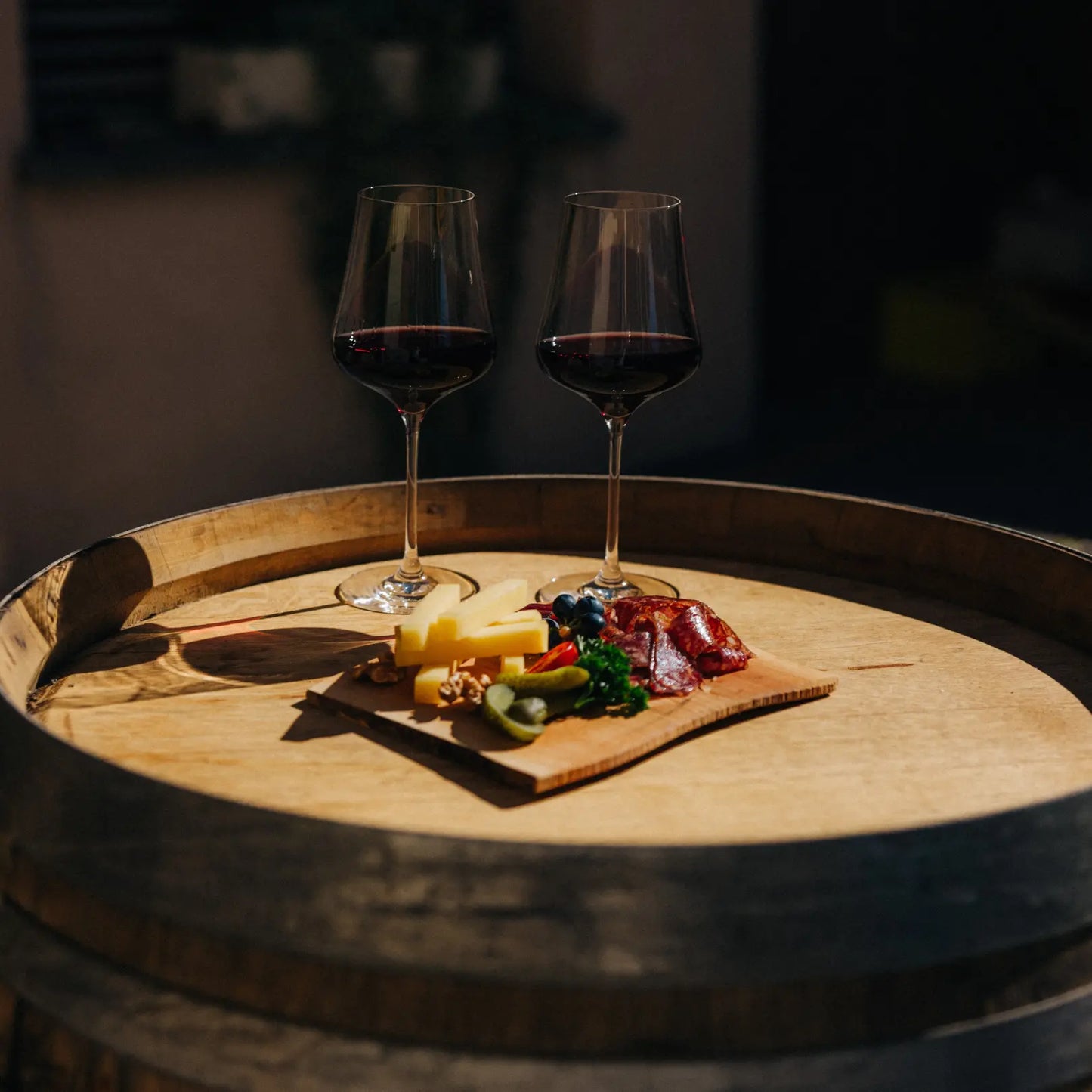 Zwei Gläser Rotwein und eine kalte Platte auf einem Holzfass bei einer Weinverkostung im Weingut Marugg