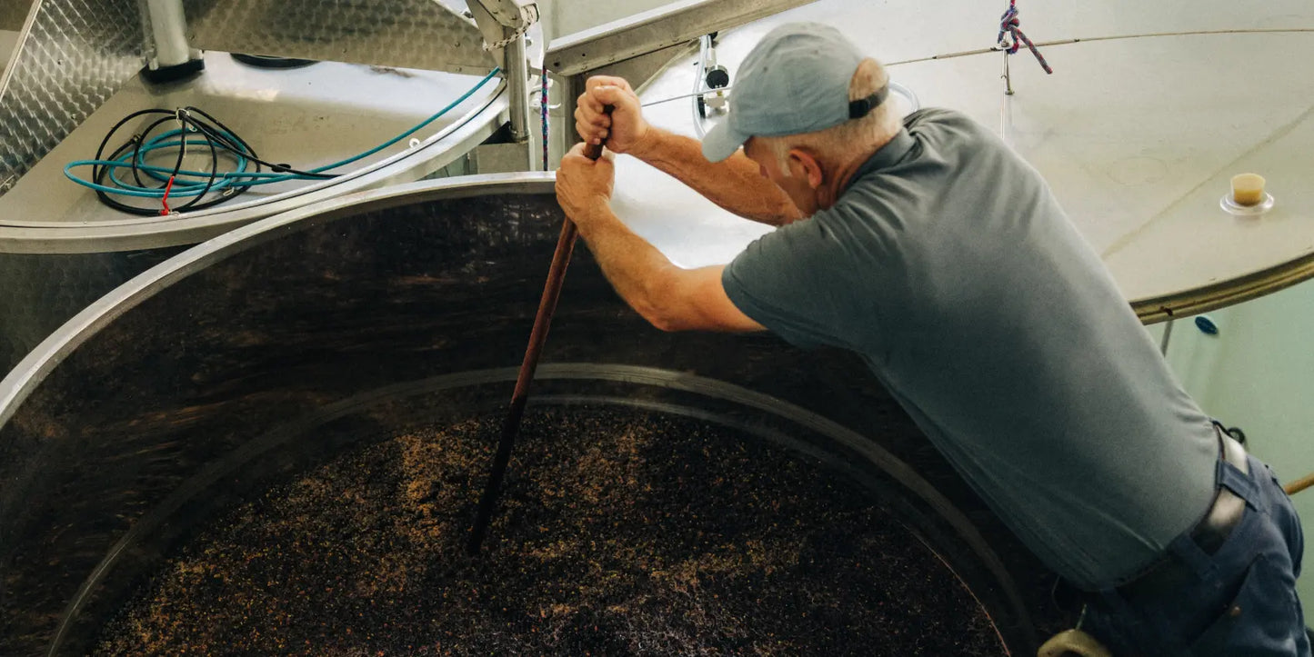 Person arbeitet im Weinkeller und rührt Traubenmaische in einem großen Edelstahltank