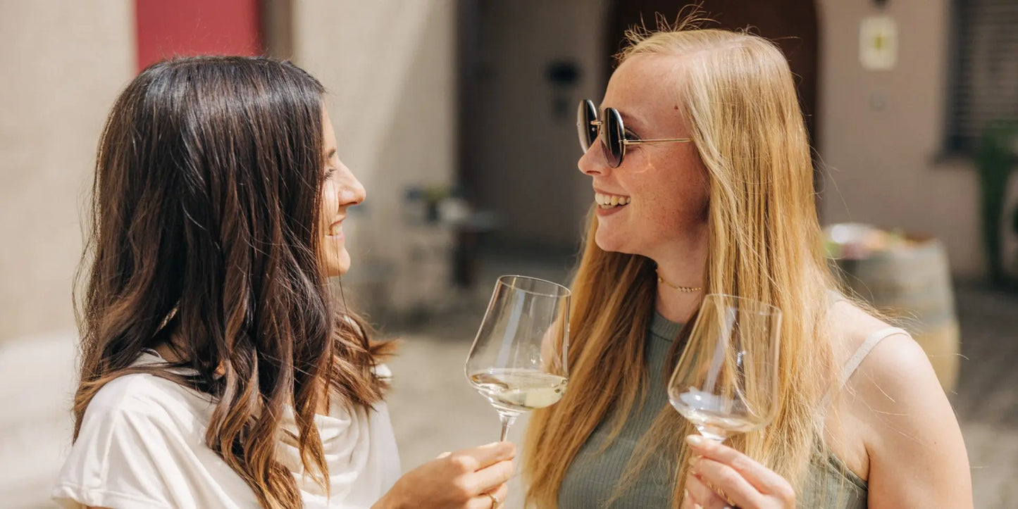 Zwei Personen stoßen mit Weingläsern im Innenhof des Weinguts Marrugg bei einer Weinverkostung an.
