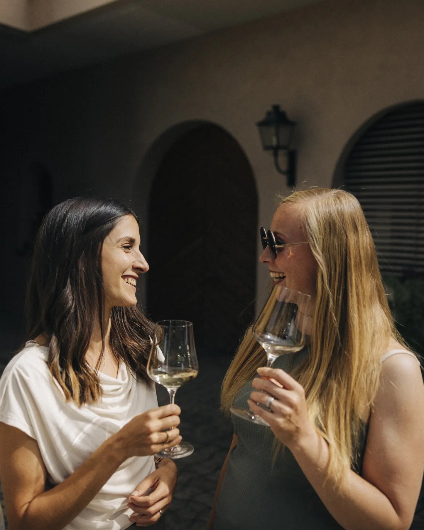 Zwei Personen stoßen mit Weingläsern im Innenhof des Weinguts bei einer Weinverkostung an.