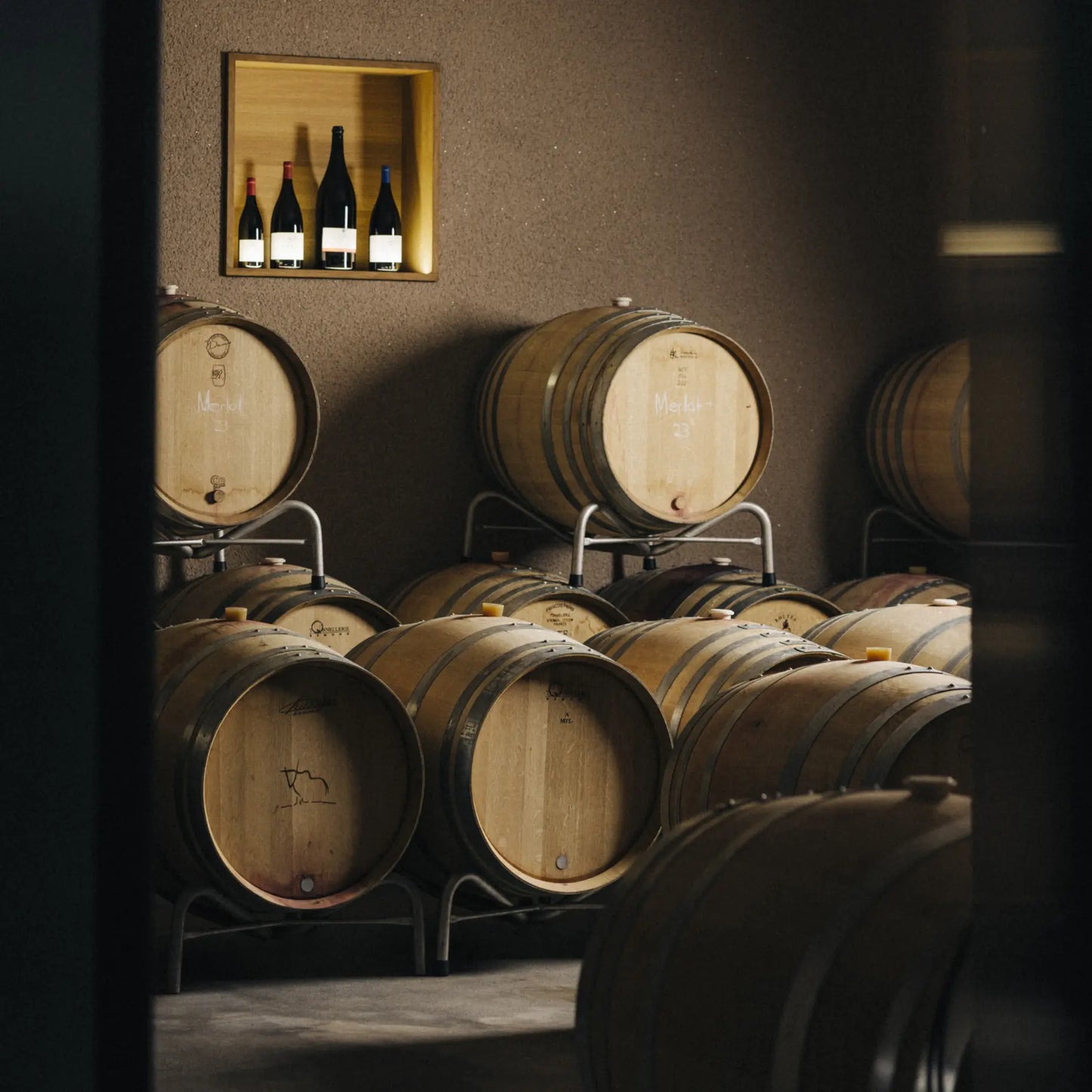 Holzfässer zur Weinreifung im Weinkeller des Weinguts, mit Flaschen im Hintergrund.