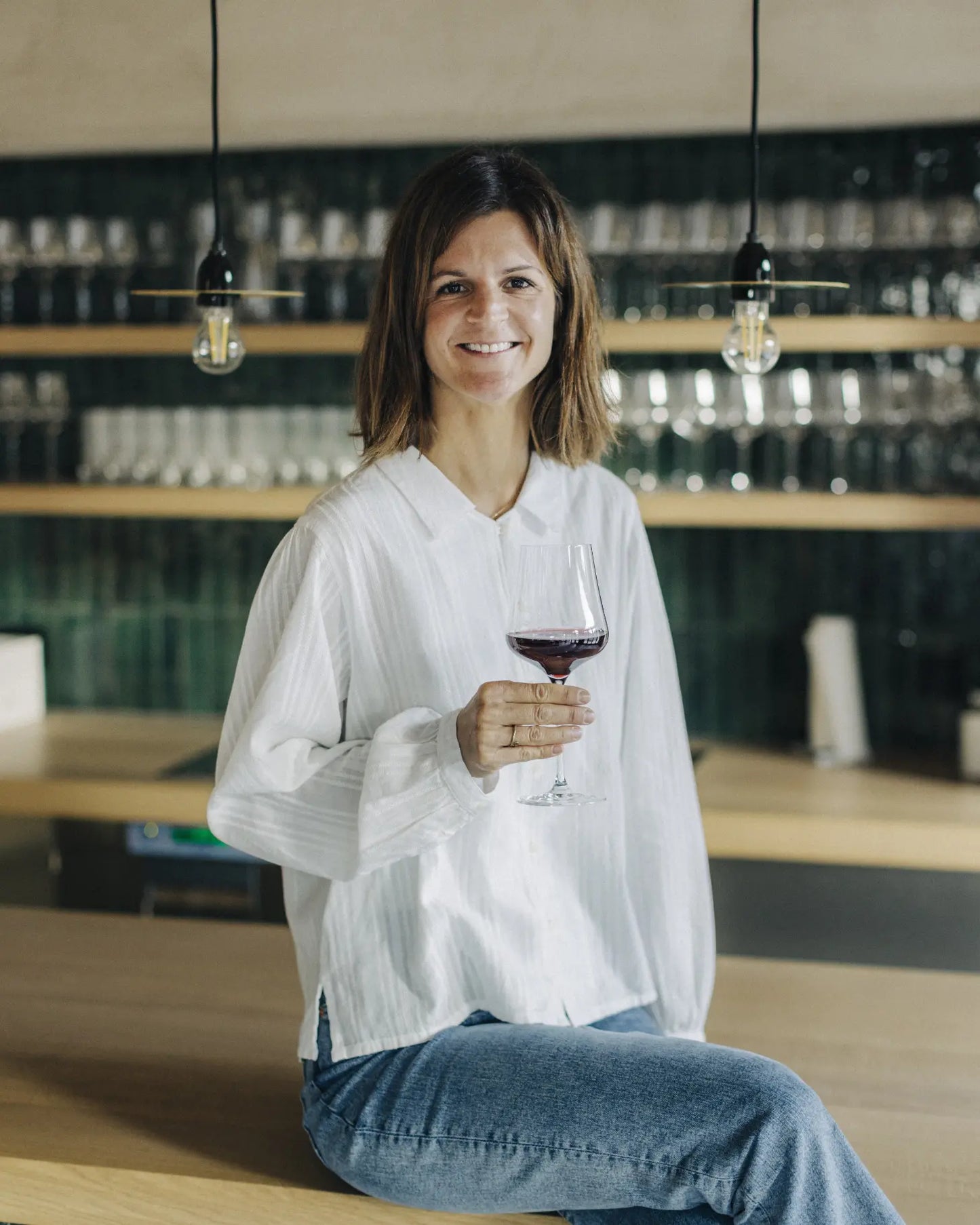 Nadja Marugg sitzt an der Bar des Weinguts Marugg und hält ein Glas Rotwein in der Hand.