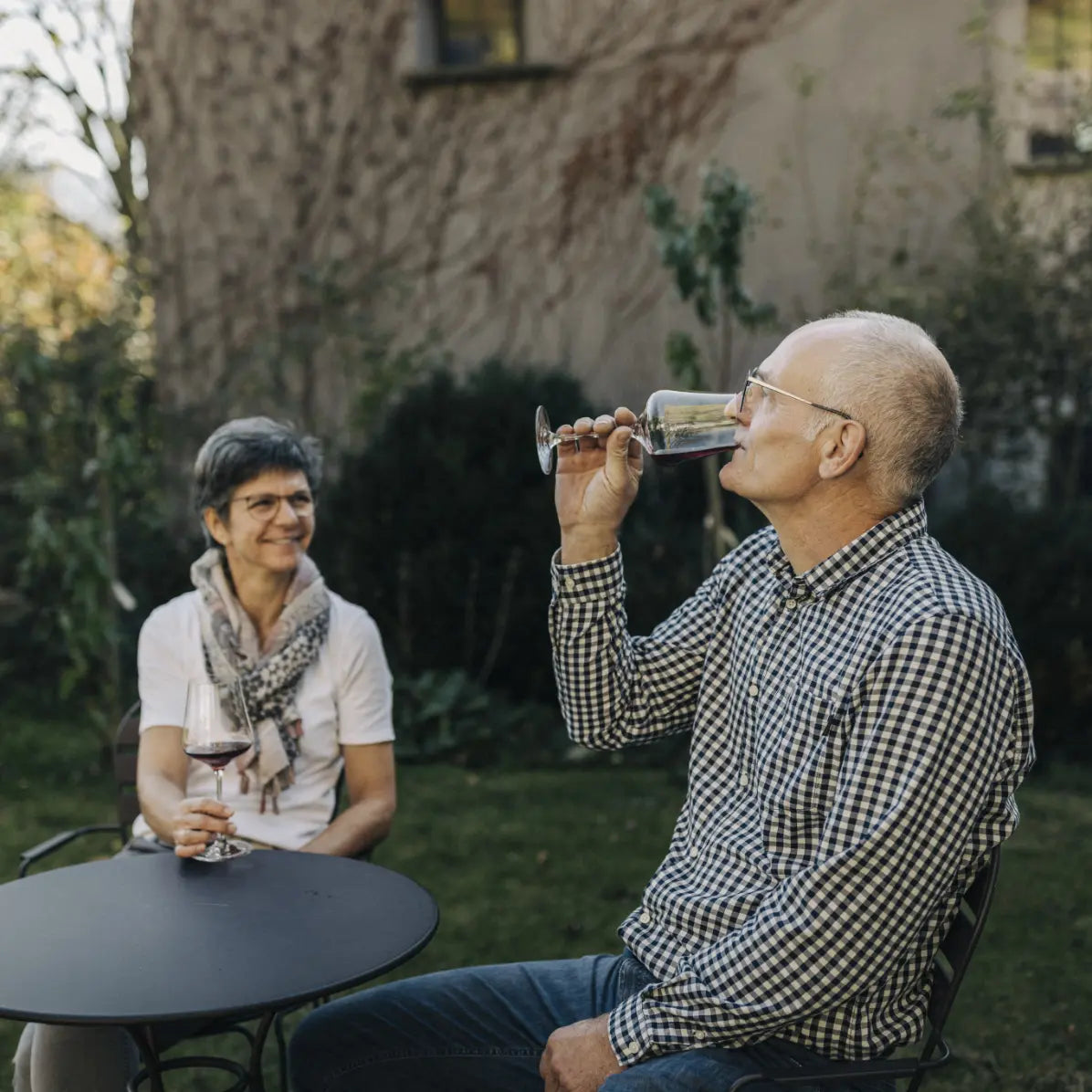 Daniel und Monika Marugg sitzen im Garten des Weinguts, eine Person trinkt Wein, die andere hält ein Weinglas.