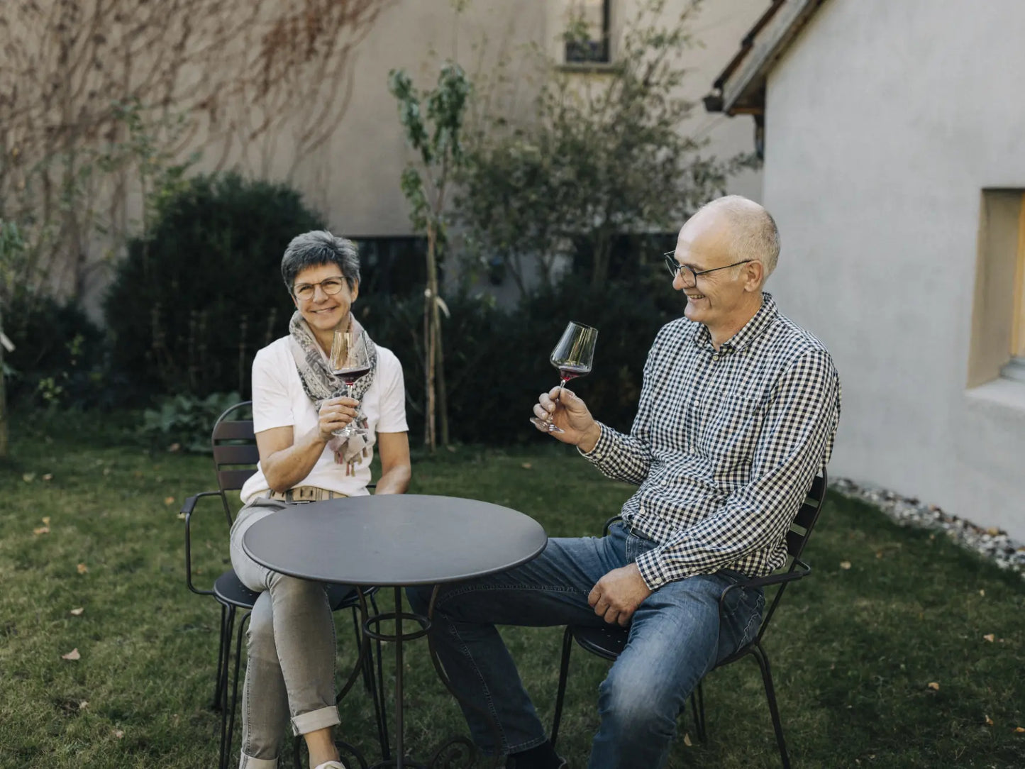 Zwei Personen sitzen im Garten des Weinguts und genießen ein Glas Wein an einem kleinen Tisch.